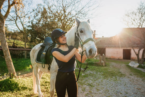 Beautiful blond woman embracing her horse after riding training at a rustic stable outdoors in Majorca stock photo