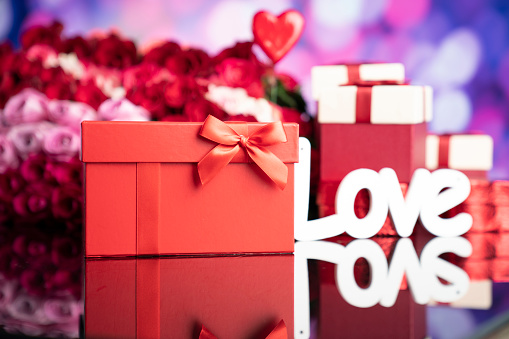 Gifts in boxes, red hearts and big bouquet of natural roses on blue bokeh background.