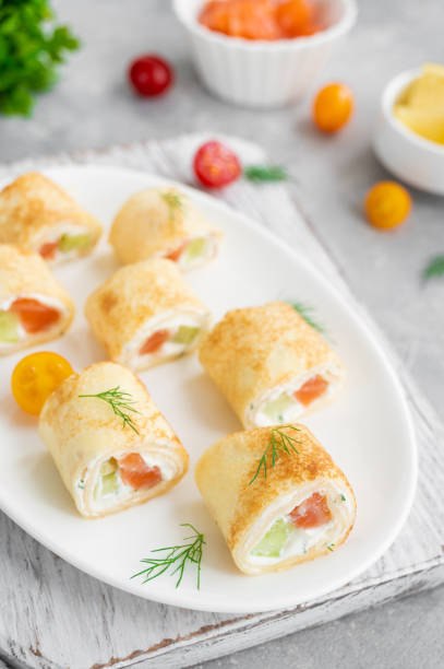 istock Thin pancake rolls or crepes rolls with smoked salmon, cream cheese, cucumber and dill on a gray concrete background. Selective focus. 1367841463