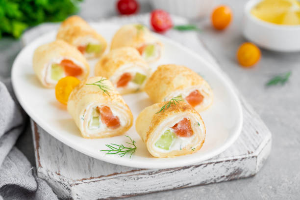 istock Thin pancake rolls or crepes rolls with smoked salmon, cream cheese, cucumber and dill on a gray concrete background. Selective focus. 1367841492