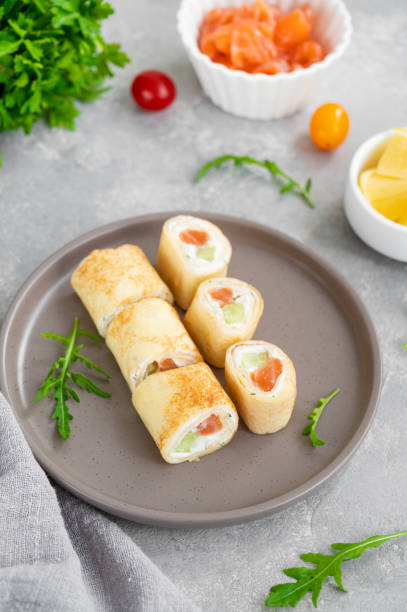 istock Thin pancake rolls or crepes rolls with smoked salmon, cream cheese, cucumber and dill on a gray concrete background. Selective focus. 1367841496