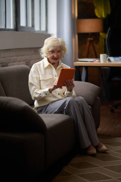 istock Woman sitting on couch looking at tablet. 1367845577