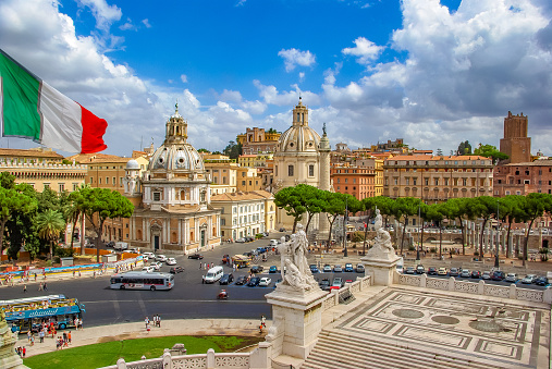 Beautiful view at Piazza Venezia with Italian flag, blue sky and sunny day with many tourists and sightseeing buses, Rome, Italy