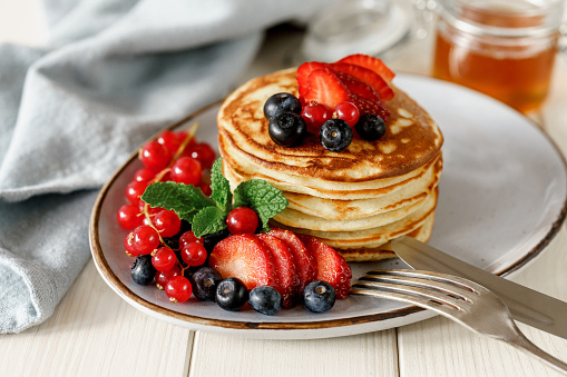 Stack of homemade pancakes with fresh blueberries, strawberries and honey