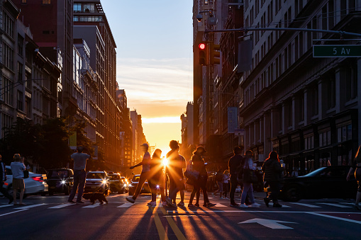 Silhouettes of men and women crossing a busy street in Midtown Manhattan, New York City with sunlight shining in the background