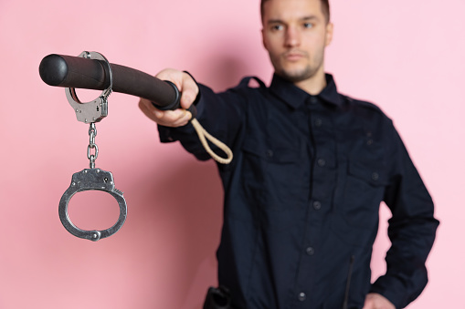 One handsome policeman officer wearing black uniform with club and handcuffs isolated on pink background. Concept of job, caree, safety. Security service. Copy space for ad