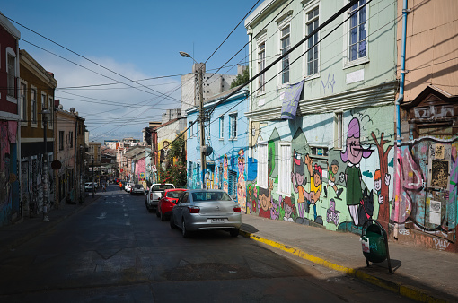 Valparaiso, Chile - February, 2020: City street in Barrio Bellavista district with colorful houses and walls decorated with graffiti. Typical street in Valparaiso with street art leading down to Ocean