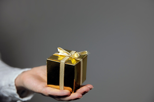 Hands holding gold gift box isolated on gray background. giving present, Birthday,Christmas,Mothersday other Holiday with copy space space for text