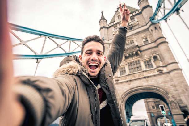 homem sorridente tirando selfie retrato durante viagem em londres, inglaterra - jovem turista homem tirando foto de férias com icônico marco da inglaterra - pessoas felizes vagando pela europa conceito - tourism travel europe northern europe - fotografias e filmes do acervo