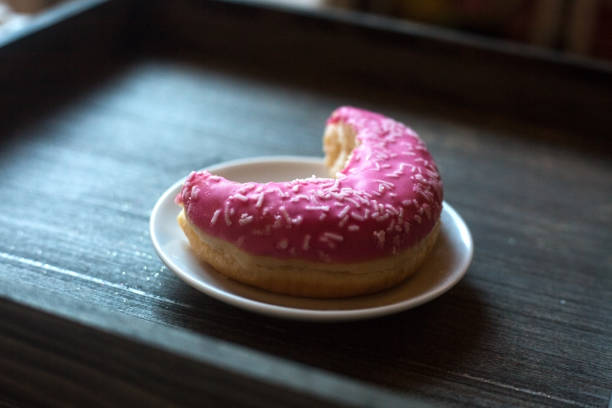 istock Side view on pink doughnut half eaten on white plate and grey wooden background 1367857027