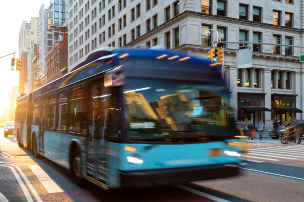 autobús de la ciudad de nueva york conduciendo por la calle 23 a través de manhattan con la luz del sol brillando entre los edificios de fondo - bus fotografías e imágenes de stock