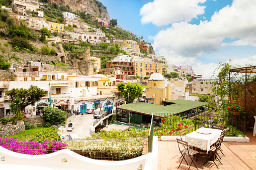 June 7, 2018. A restaurant balcony in front of the terraced buildings hugging the hills of the beach town of Positano, on the Amalfi Coast in Italy on a bright sunny day.