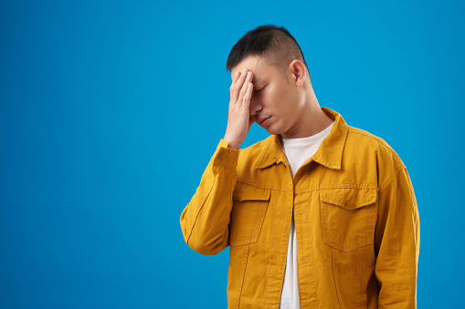 Tired disappointed young man making face palm gesture, isolated on blue