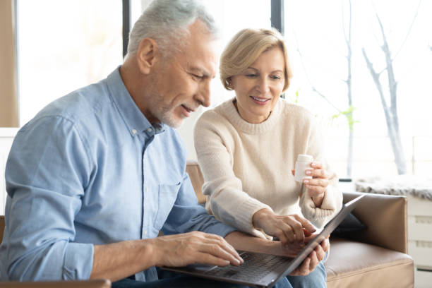 senior couple with pills and laptop in living room - laptop mature adult senior adult old imagens e fotografias de stock