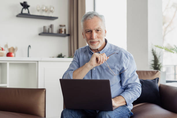 istock Smiling elderly man with laptop looking at camera 1367863317