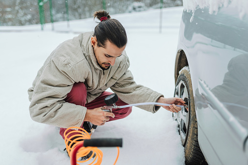 Young man Checking Tire Pressure during winter