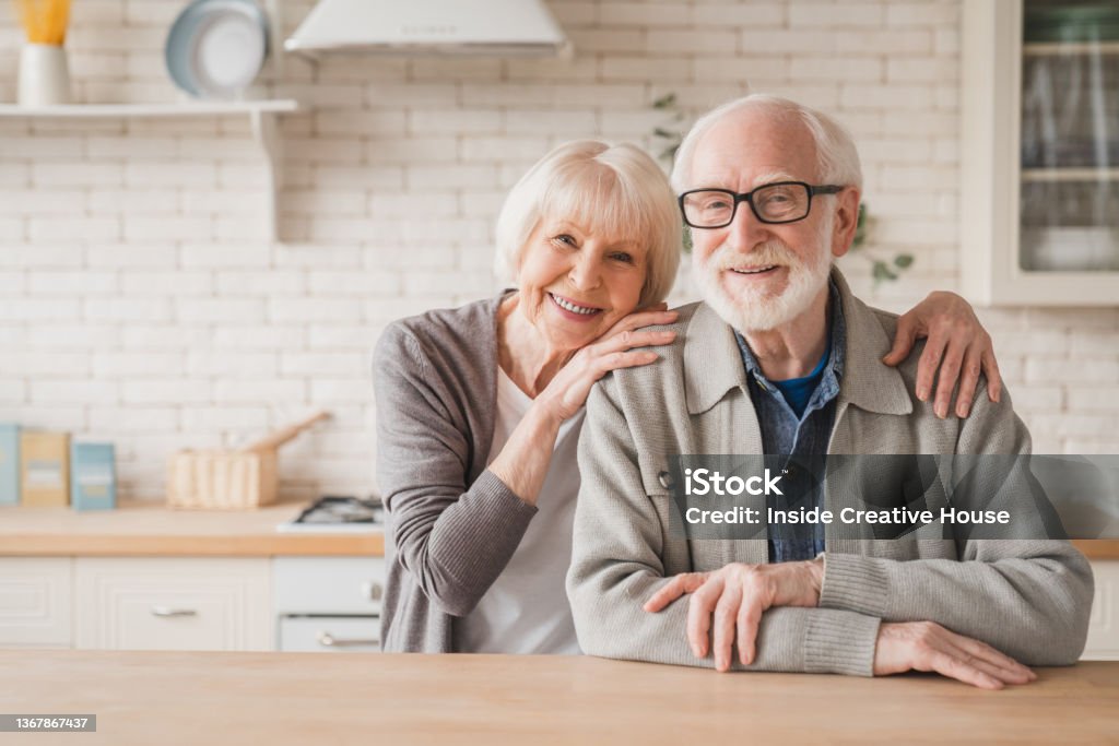 Portrait of caucasian smiling senior old elderly couple family spouses grandparents looking at camera, embracing hugging with love and care at home kitchen Senior Adult Stock Photo