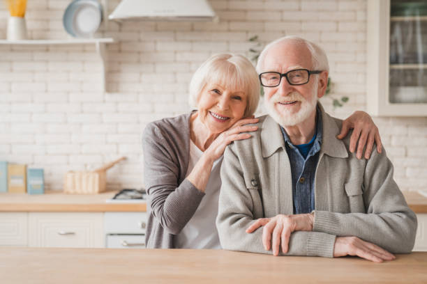 portrait of caucasian smiling senior old elderly couple family spouses grandparents looking at camera, embracing hugging with love and care at home kitchen - senior couple imagens e fotografias de stock