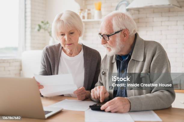 Serious Caucasian Old Elderly Senior Couple Grandparents Family Counting Funds On Calculator Doing Paperwork Savings Paying Domestic Bills Mortgage Loan Pension At Home Using Laptop Stock Photo - Download Image Now