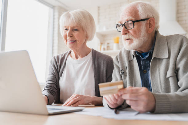 vieux âgés intelligents couple de caucasiens grands-parents mari et femme recevant une pension payer des factures domestiques, faire des achats en ligne avec carte de crédit et ordinateur portable, services bancaires électroniques et commerce électron - senior couple senior adult pension couple photos et images de collection