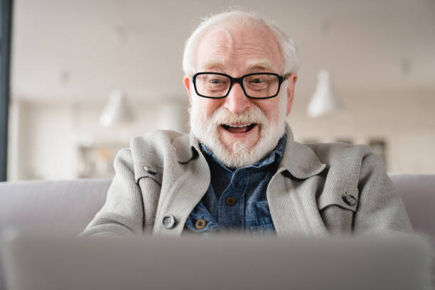 コメディ、映画を見るためにラップトップを使用して、親戚とオンラインでビデオ通話で話し、ソファの距離に取り組む陽気な笑っている先輩老人の祖父のクローズアップトリミング肖像画 - one senior man only grandfather portrait old ストックフォトと画像