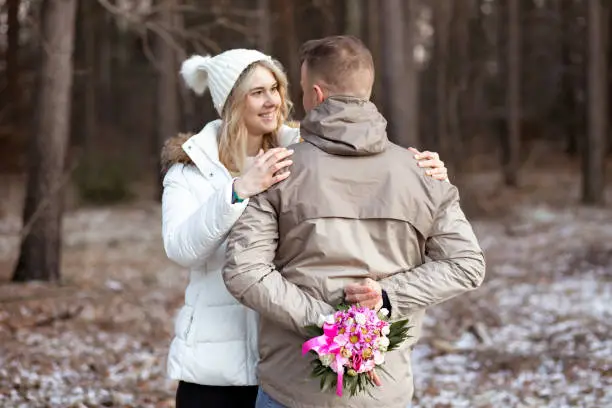 Photo of Portrait of two people couple fair-haired woman and man hugging together hiding flowers outdoors in frost weather street