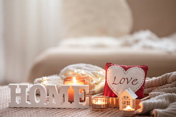 A cozy composition with candles and a decorative word home on a blurred background in the interior of a room, valentine's day concept.
