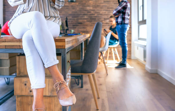 Unrecognizable businesswoman sitting on table in the office Unrecognizable businesswoman sitting on table in the office with colleagues working in the background woman sitting cross legged in chair stock pictures, royalty-free photos & images