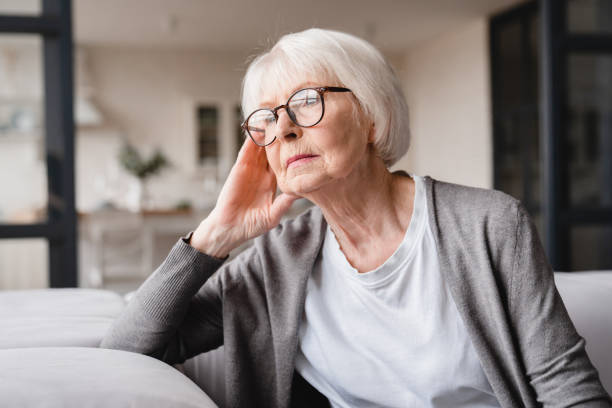 悲しい疲れた病気の孤独な失望した白人の高齢の高齢の女性の祖母は、ソファのソファに座って、ノスタルギー、痛み、行方不明の孫、倒産、自宅での詐欺を感じる - dementia ストックフォトと画像