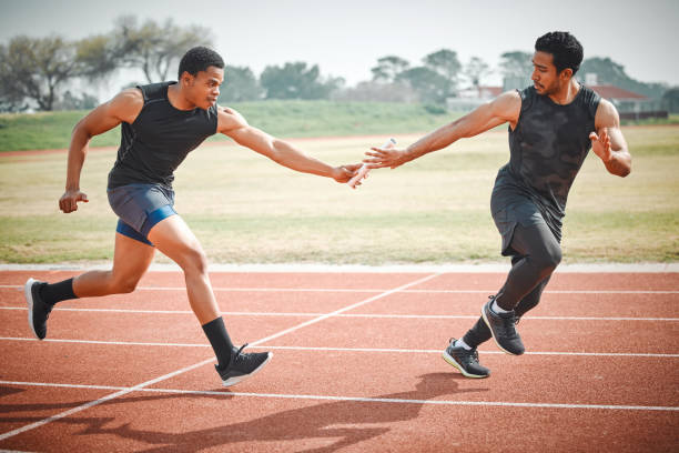 Full length shot of a handsome young male athlete grabbing a baton from his teammate during a relay race The handover relay stock pictures, royalty-free photos & images