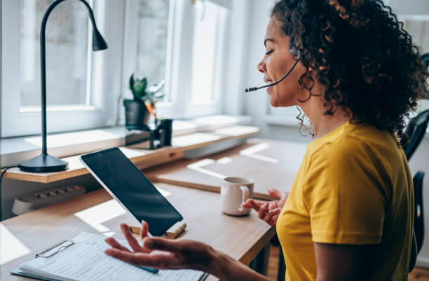 Businesswoman using tablet and headset in the office. Shot of a young woman using a digital tablet and headset while working from home. Beautiful young woman having video call in the office. Shot of an attractive woman using a tablet for video conference. voip stock pictures, royalty-free photos & images