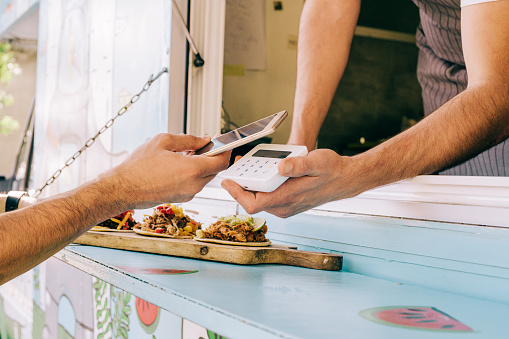 Shot of male customer using smart phone for buying food from food truck. Young man doing contactless payment for tasty tacos. A client making wireless or contactless payment using smart phone.