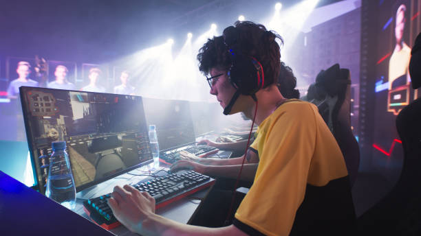 Teen gamer playing shooter with team Esportsman gamer in glasses and headphones playing shooter on computer near team while taking park in professional gaming championship battle facilities protection services stock pictures, royalty-free photos & images