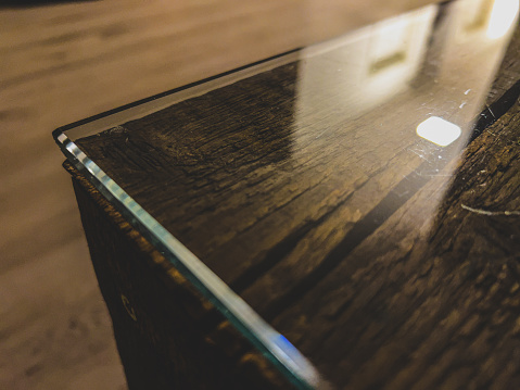 A table edge of a wooden table with glass top.