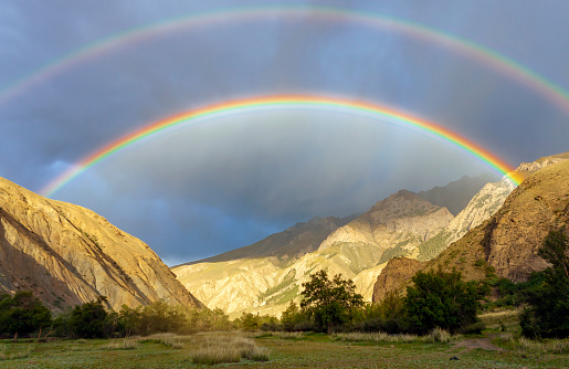 Rare double rainbow in the dark sky in the mountains.