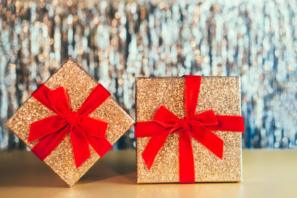 caixas de presente douradas brilhantes com fita vermelha de veludo com um arco no fundo de lata de ouro brilhante. o conceito de presente de aniversário, dia dos namorados, natal, ano novo. fundo festivo. - bow christmas red velvet - fotografias e filmes do acervo