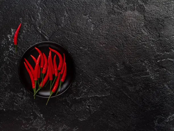 Photo of Chili peppers on a black plate, on a black background. View from above.