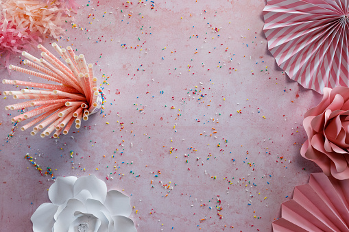 Copy space shot of pastel pink background with some paper decor on it, drinking straws and colorful sprinkles scattered all around.