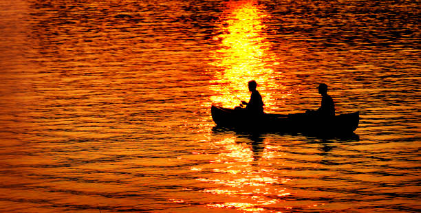 日没または日の出時に湖川のカヌー釣りの2人 - city of sunrise 写真 ストックフォトと画像