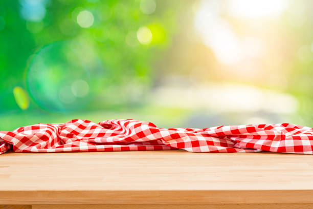 istock Table with crumpled picnic blanket and lush foliage background 1367883476
