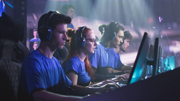 Gamers with trainer playing videogame Young and successful men and women professional gamers with coach playing video game on computers against monitor with match broadcast during esports tournament facilities protection services stock pictures, royalty-free photos & images