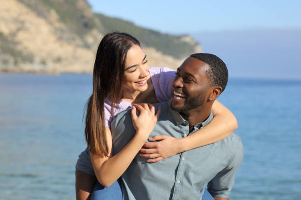 istock Funny interracial couple on piggyback on the beach 1367884591