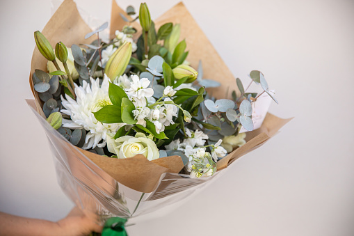 Big bouquet of mixed white and green flowers, held against white wall.
