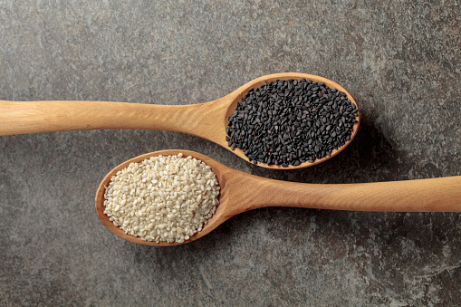 Wooden spoons with black and white sesame seeds on a stone background. Top view.