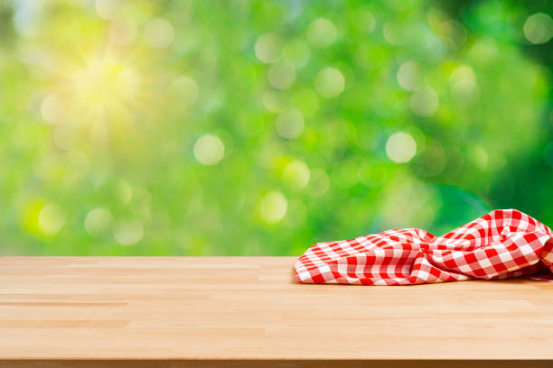 istock Table with crumpled picnic blanket and lush foliage background 1367887497