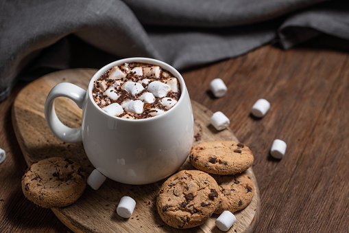 Mug of a fragrant hot chocolate or coffee with marshmallows and cookies on a wooden table