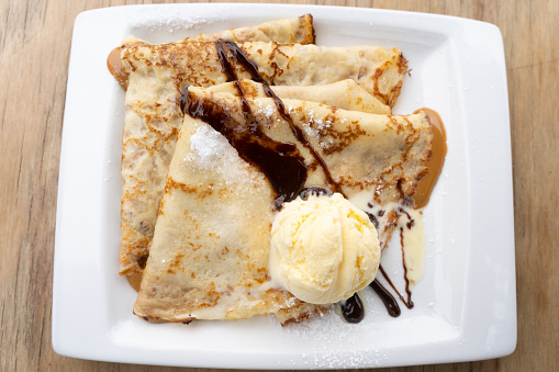 Top view of caramelized condensed milk crepes plate with vanilla ice cream, chocolate and icing sugar. Sweet dessert concept