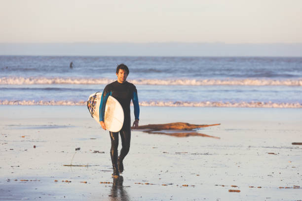 サーフボードを持ってビーチを歩く若い白人の男。 - oregon beach ストックフォトと画像