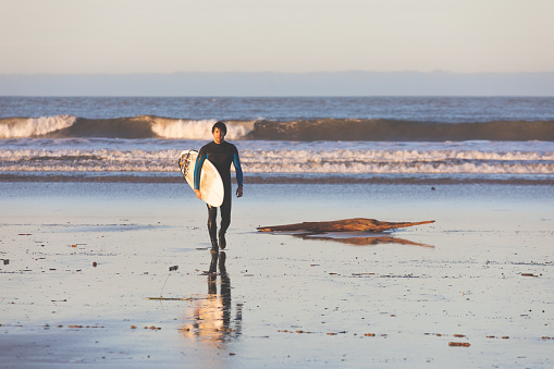 Young caucasian man walking on the beach with a surfboard.