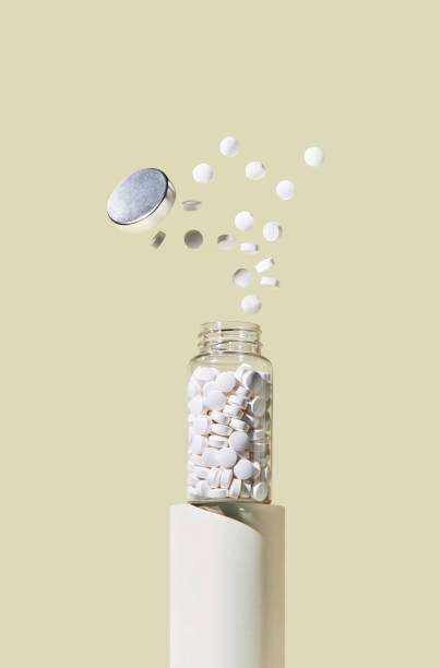 белые таблетки вылетают из стеклянной банки на пастельно-желтом фоне. - pill bottle bottle medicine white стоковые фото и изображения